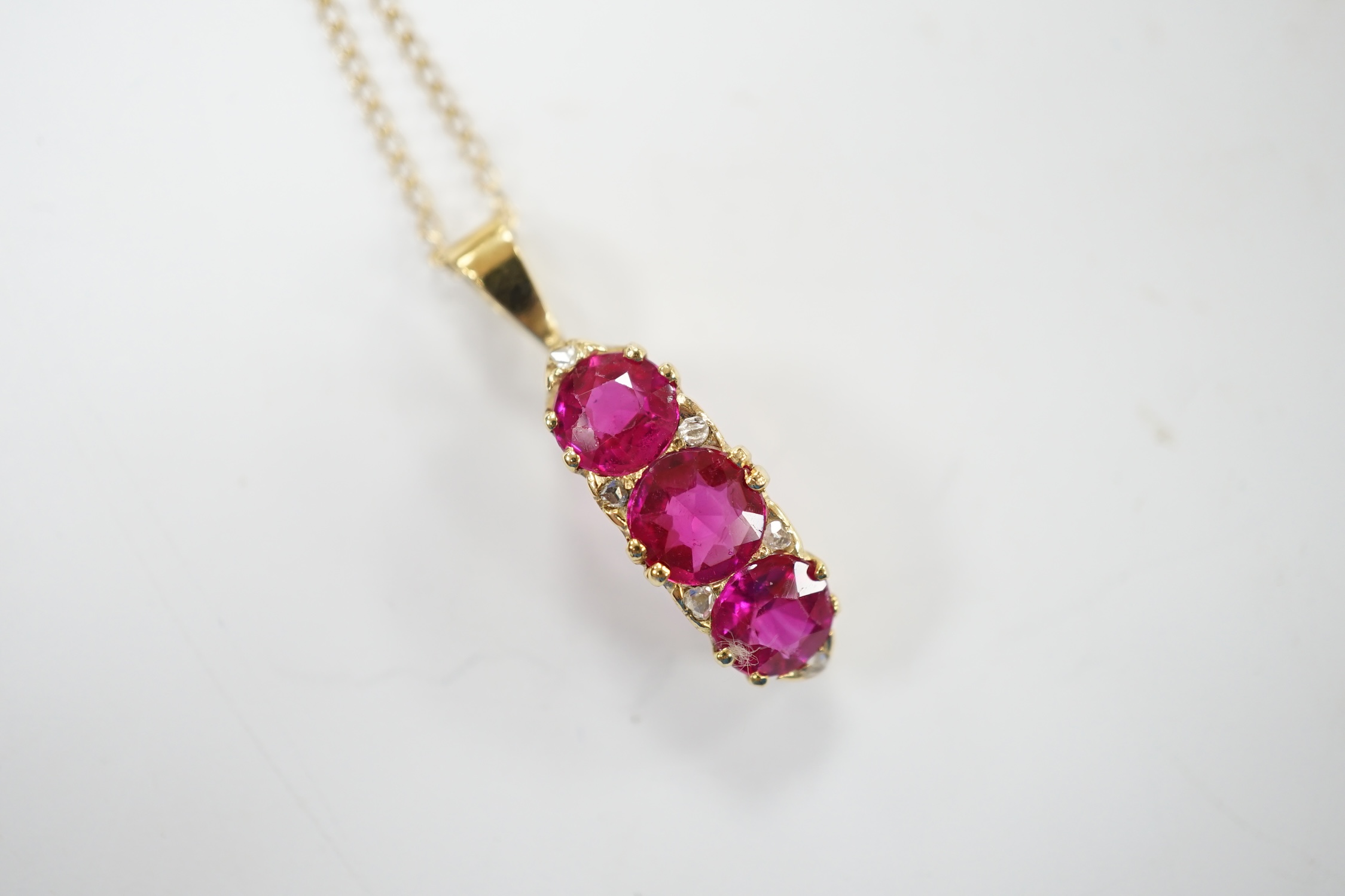 A modern 18ct gold and three stone synthetic ruby set curved pendant, with diamond chip set spacers, overall 27mm, on a 375 chain, 48cm, gross weight 4.8 grams. Fair condition.